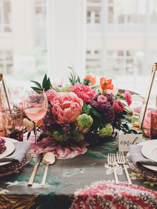 Table set with blue and pink tablecloth, white plates, gold flatware, gold candlesticks and pink flowers.